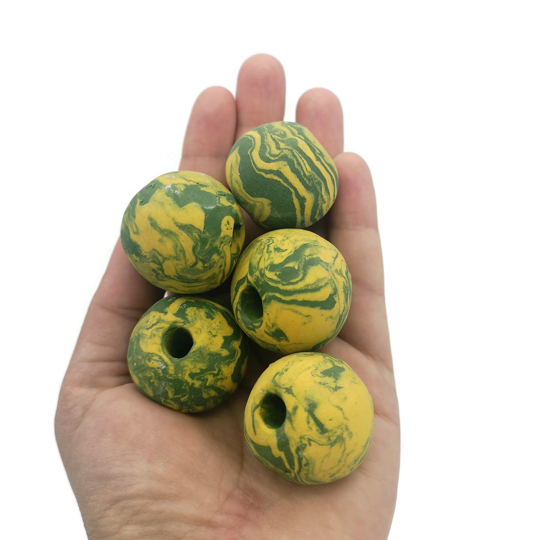 Hand holding 5 large green and yellow beads with large holes on a white background