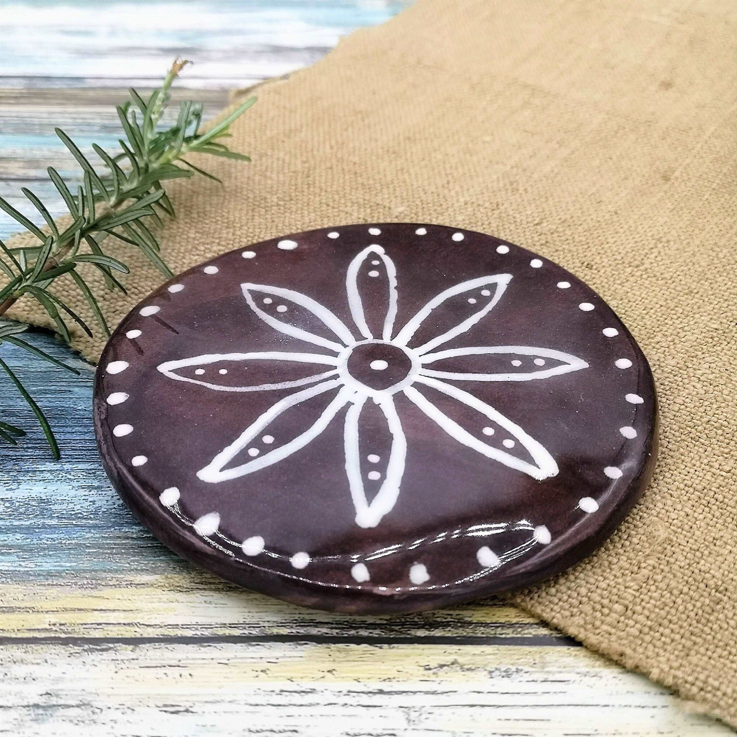 Handcrafted Ceramic coaster tile, round, with handpainted white floral motif on a brown background.